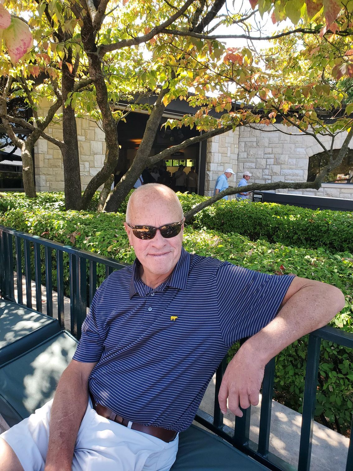 A man wearing sunglasses is sitting on a bench with his arm resting on a railing.