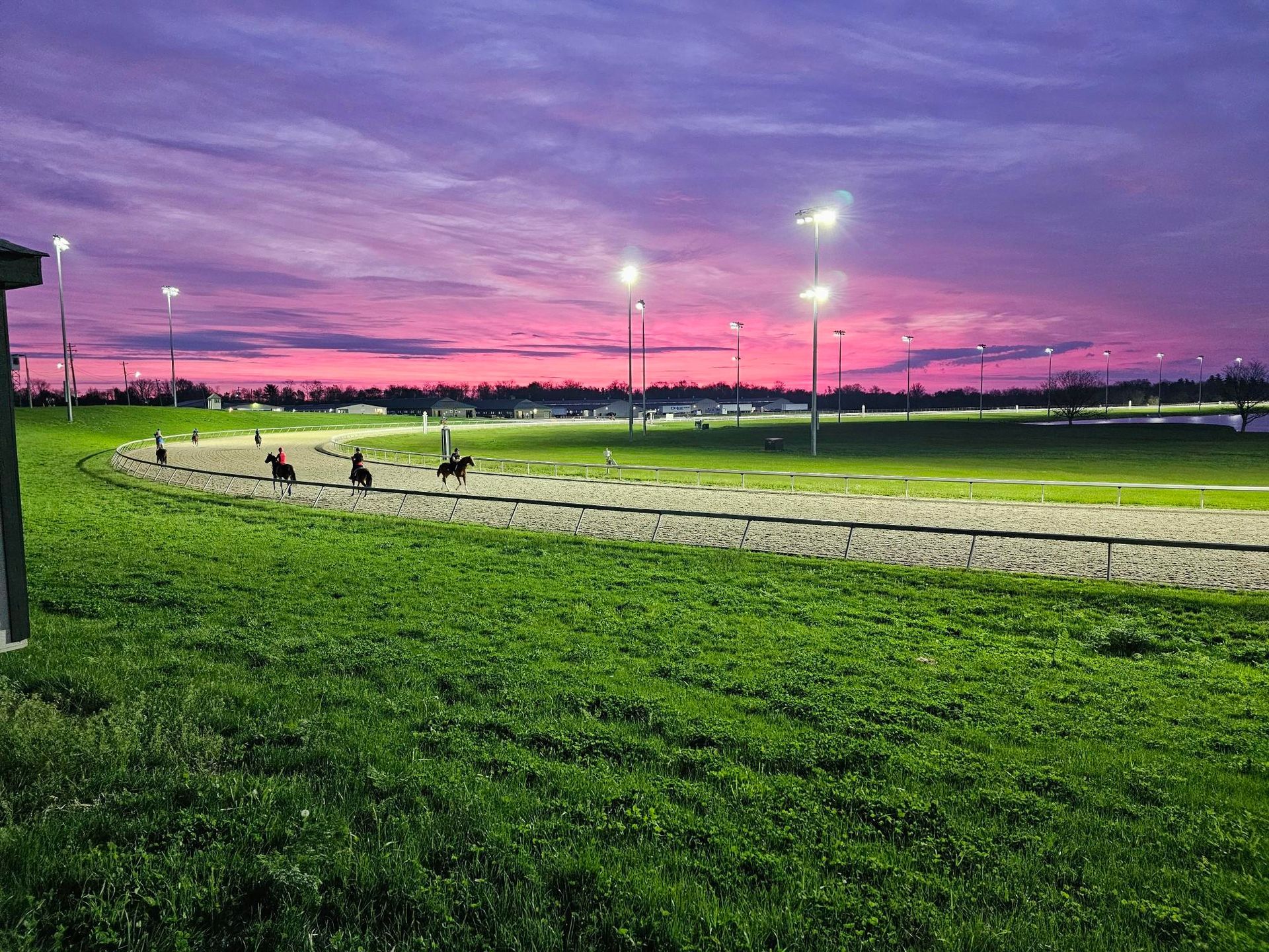 A sunset over a race track with horses running on it.