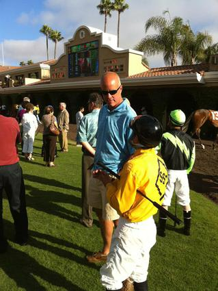 A man in a blue shirt is talking to a jockey in a yellow shirt