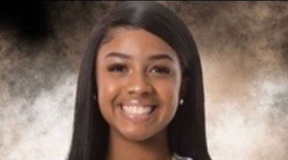 A woman in a jumpsuit is leaning against a column.