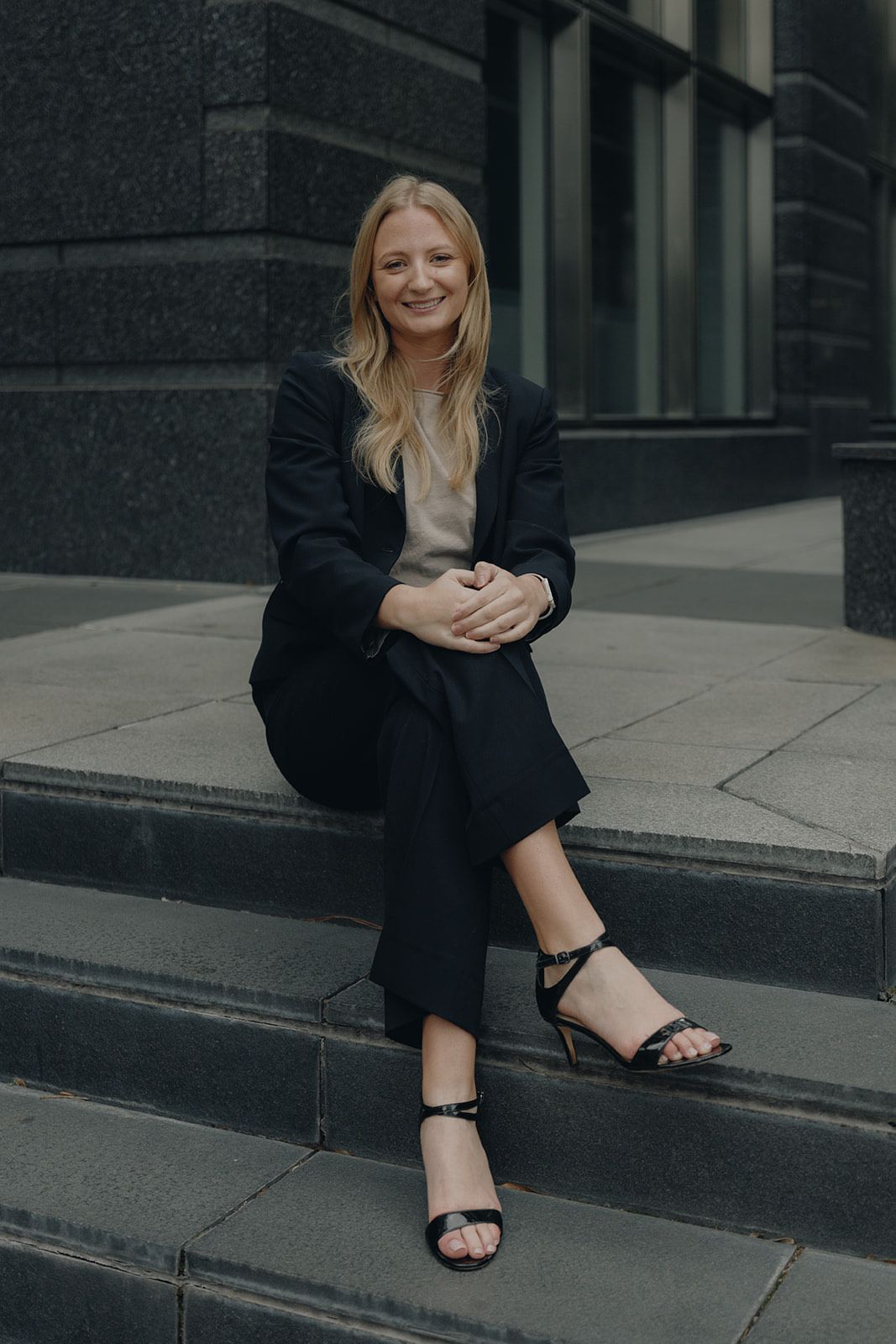 A woman in a jumpsuit is leaning against a column.