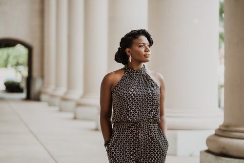 A woman in a jumpsuit is standing in front of a row of columns.