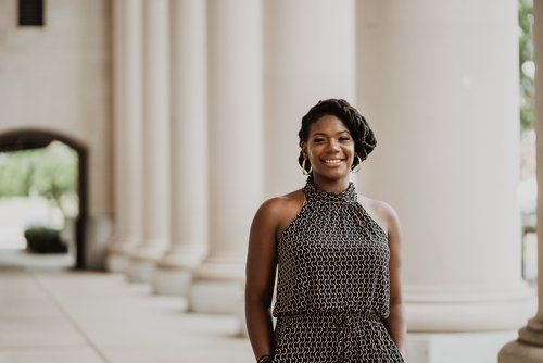 A woman is standing in front of a row of columns.