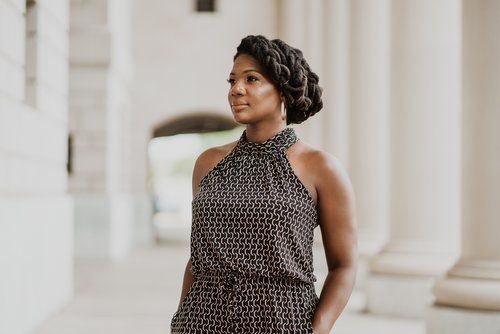 A woman in a dress is standing in front of a building with columns.