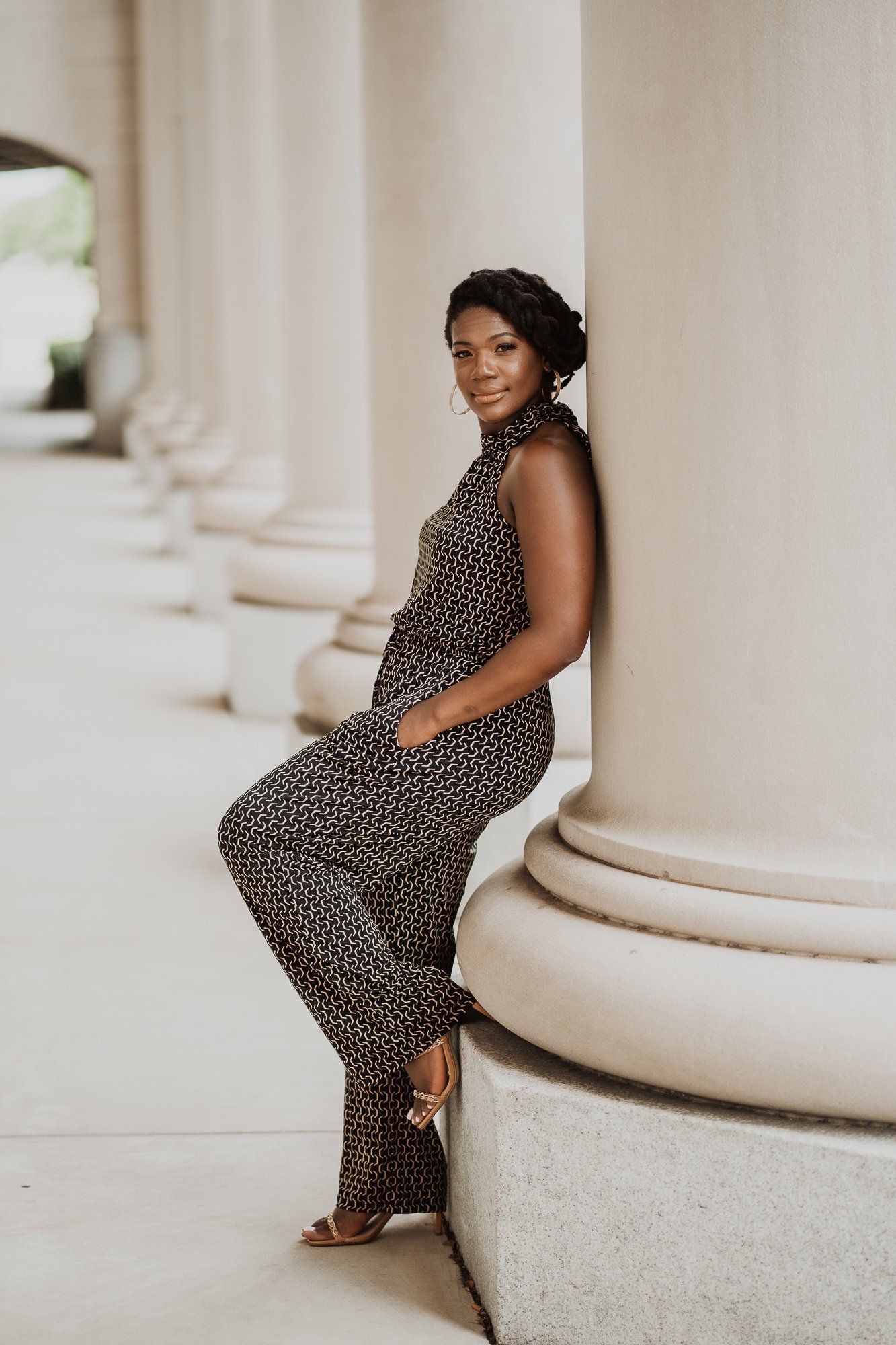 A woman in a jumpsuit is leaning against a column.