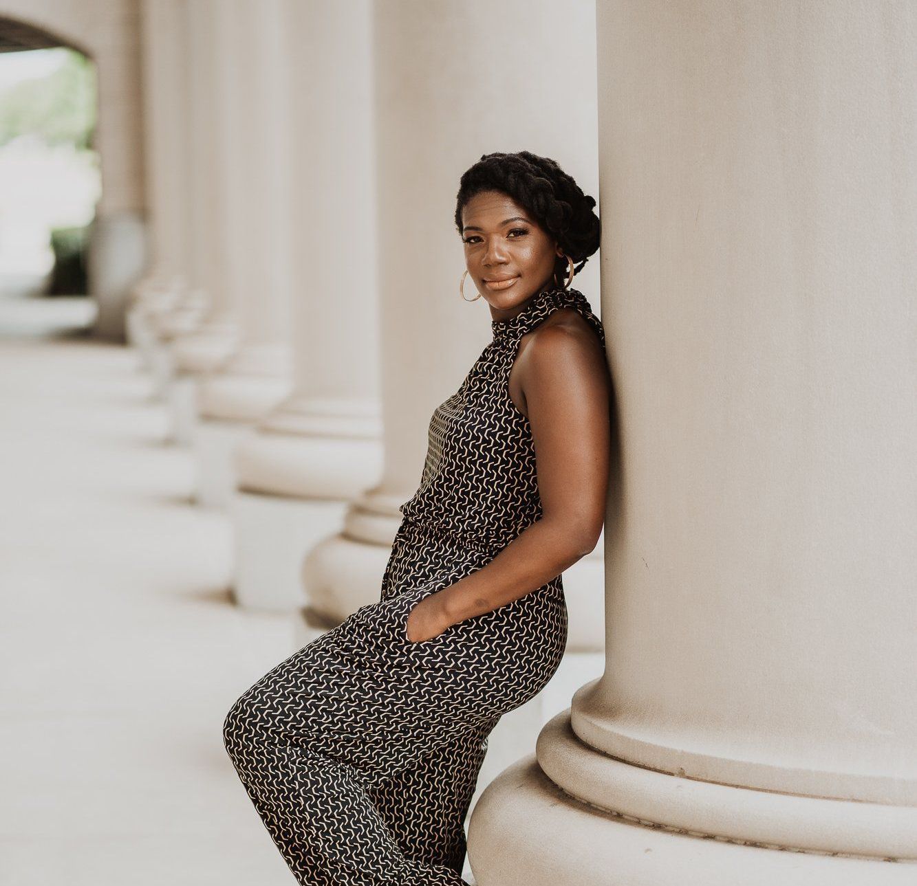 A woman leaning against a column with her hands in her pockets
