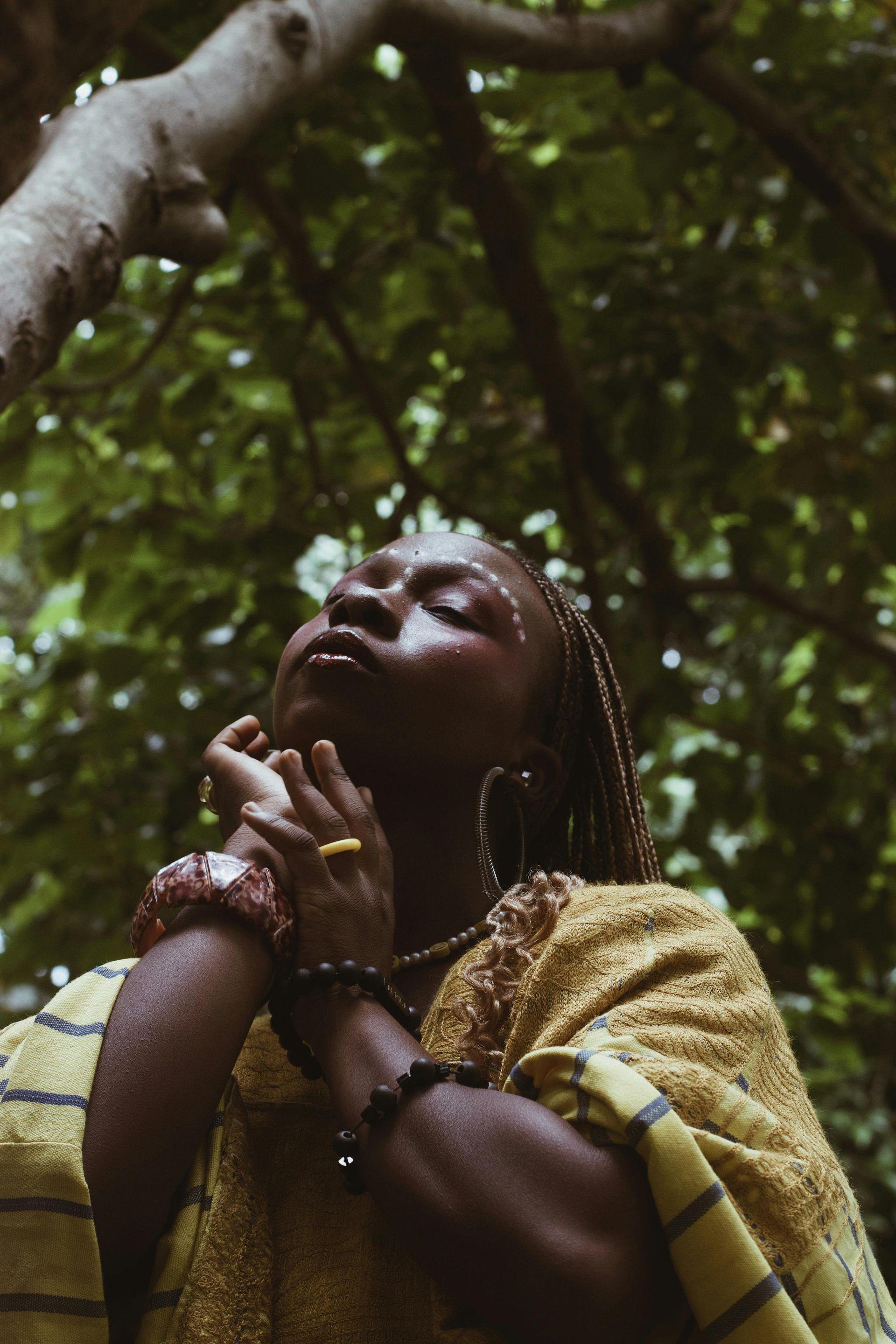 A woman is standing under a tree with her hands on her face.