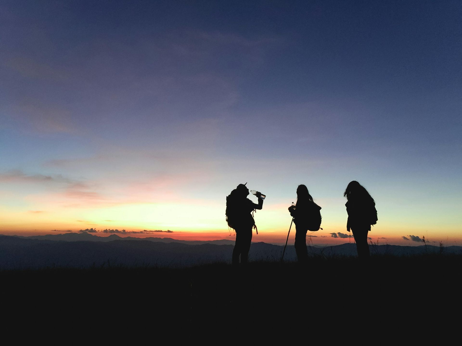 Three people standing on top of a hill at sunset