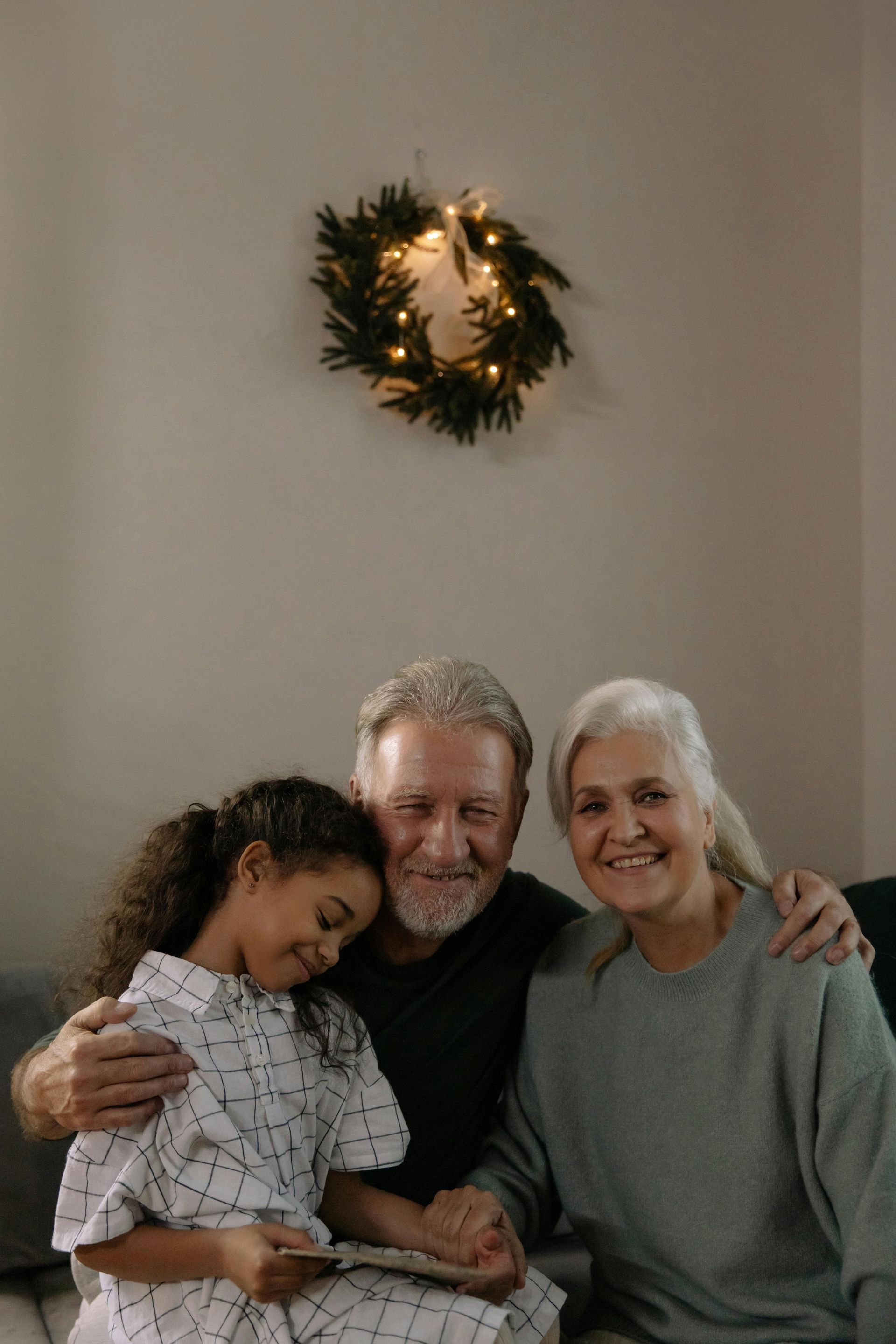 An elderly couple and a young girl are sitting on a couch.