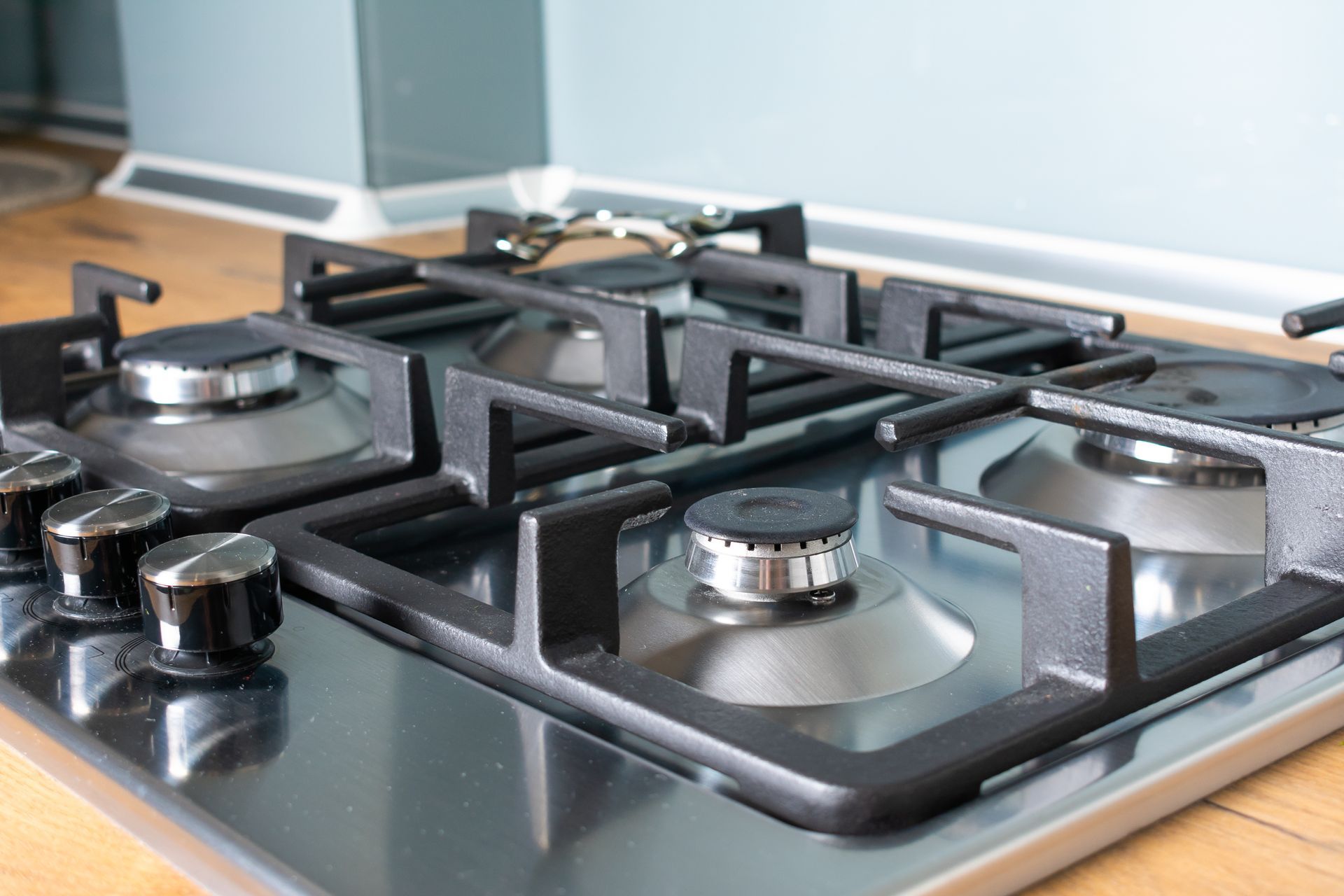 Stainless steel gas stovetop with black grates and knobs on a wooden counter.