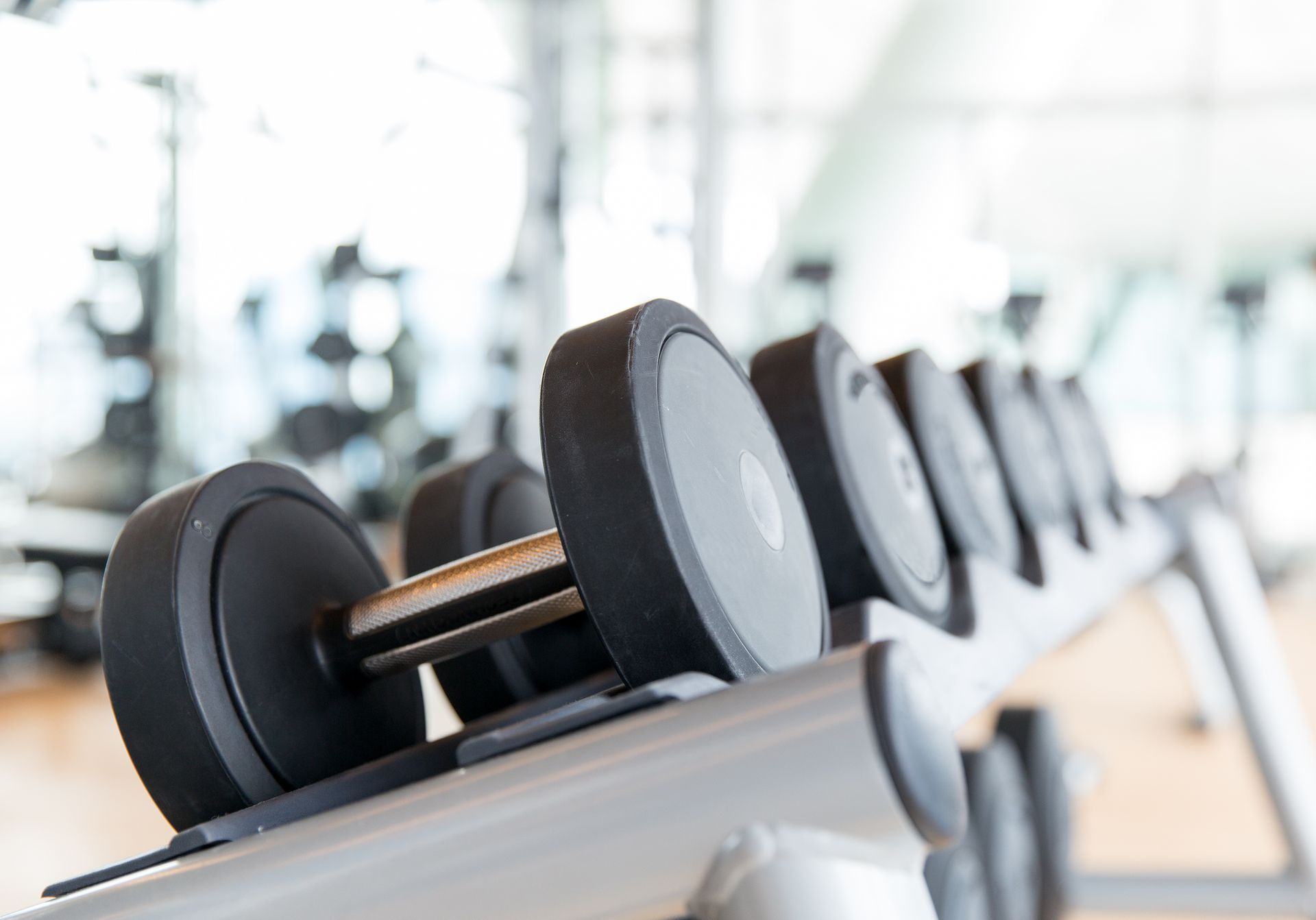 Dumbbells arranged on a rack in a gym, with blurred background of other equipment.