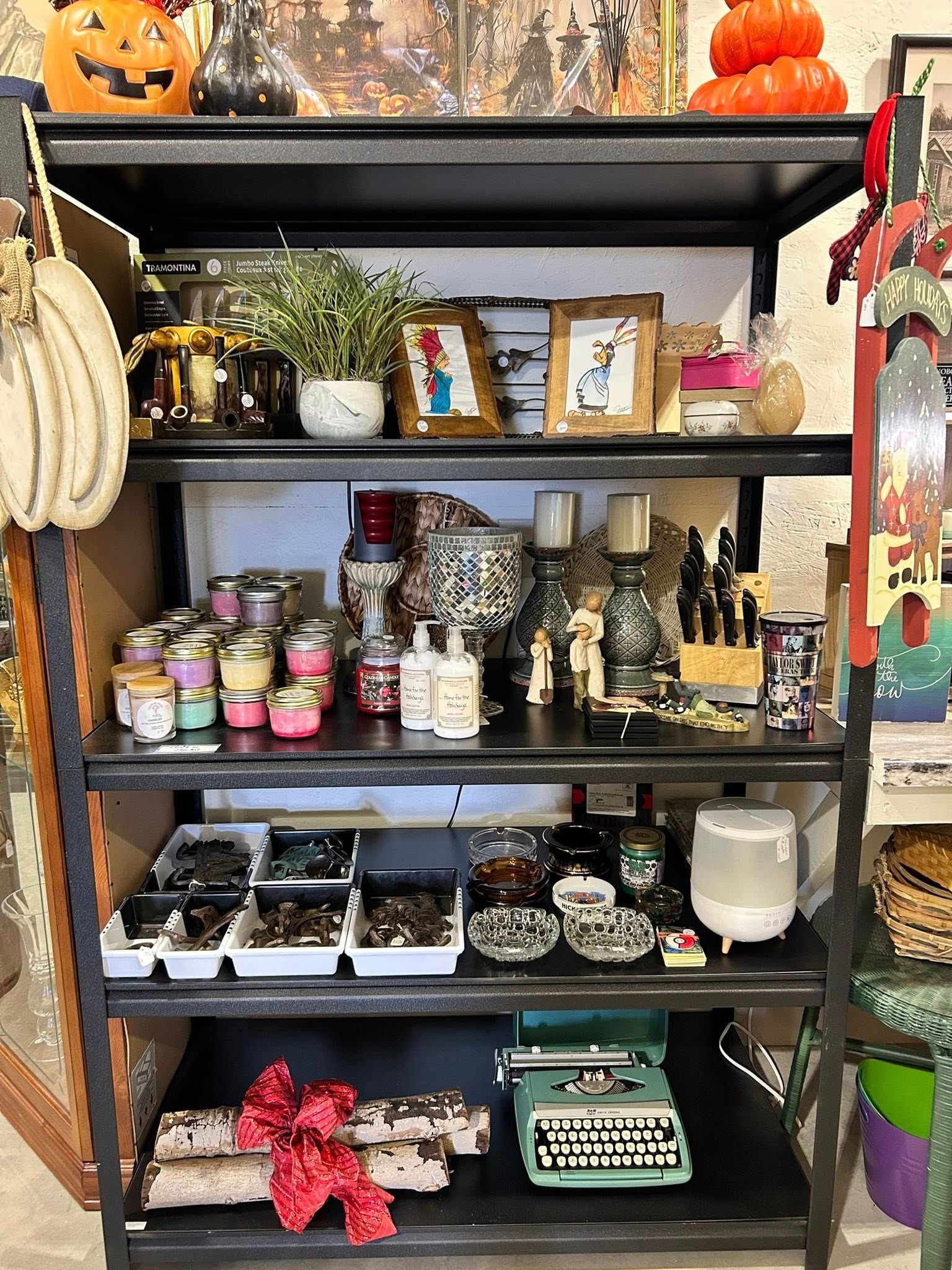 Shelves of decor and gifts: pumpkins, candles, plants, typewriter, birch logs with red bow.