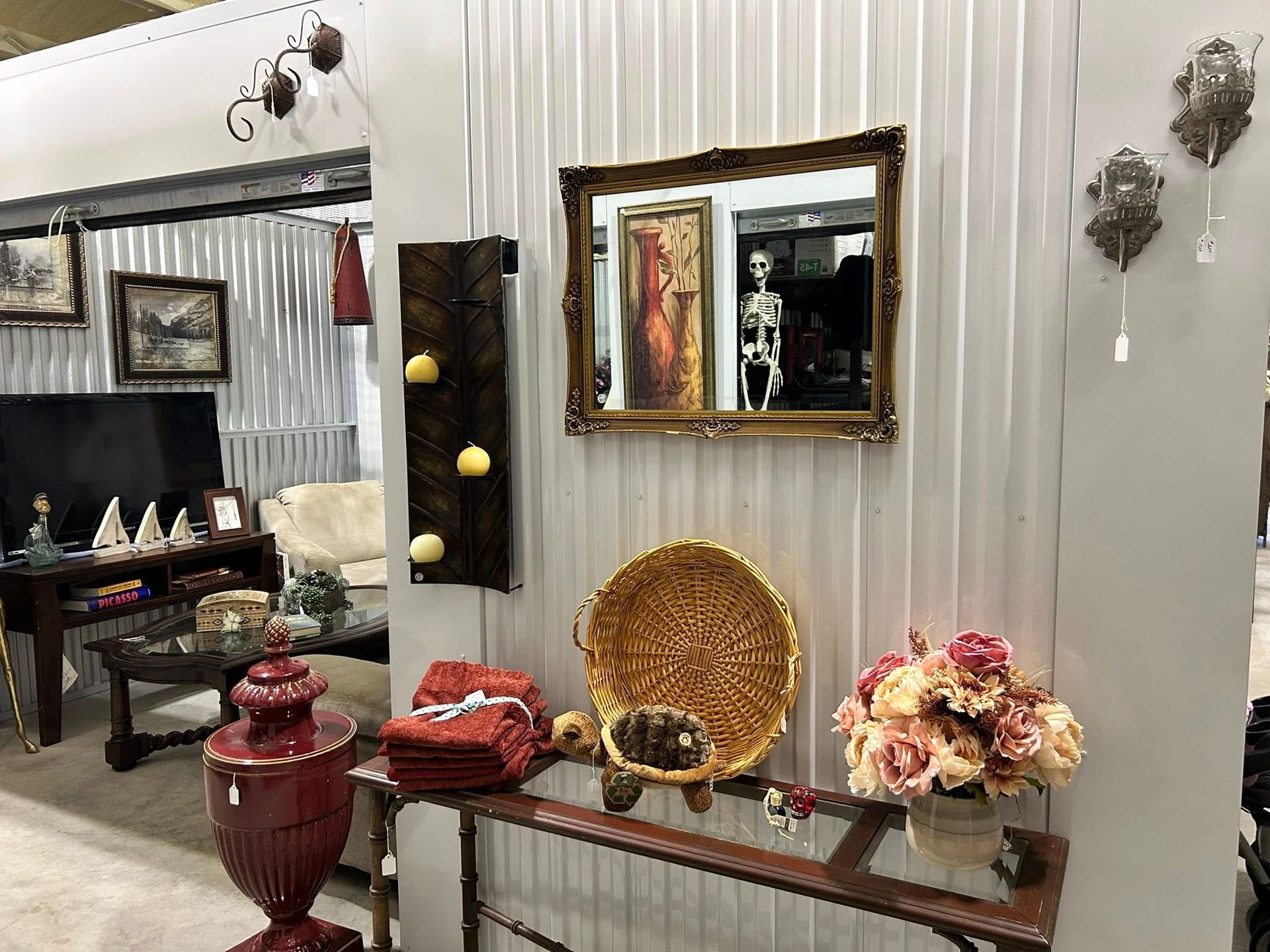 Display of decorative items, including a mirror, basket, flowers, and a vase, on a shelf against a textured wall.
