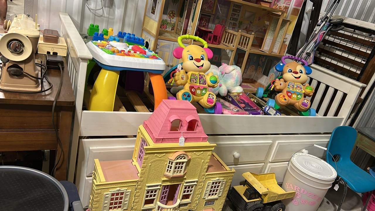 Toys and other items, including a toy house and baby toys, clutter a white dresser.