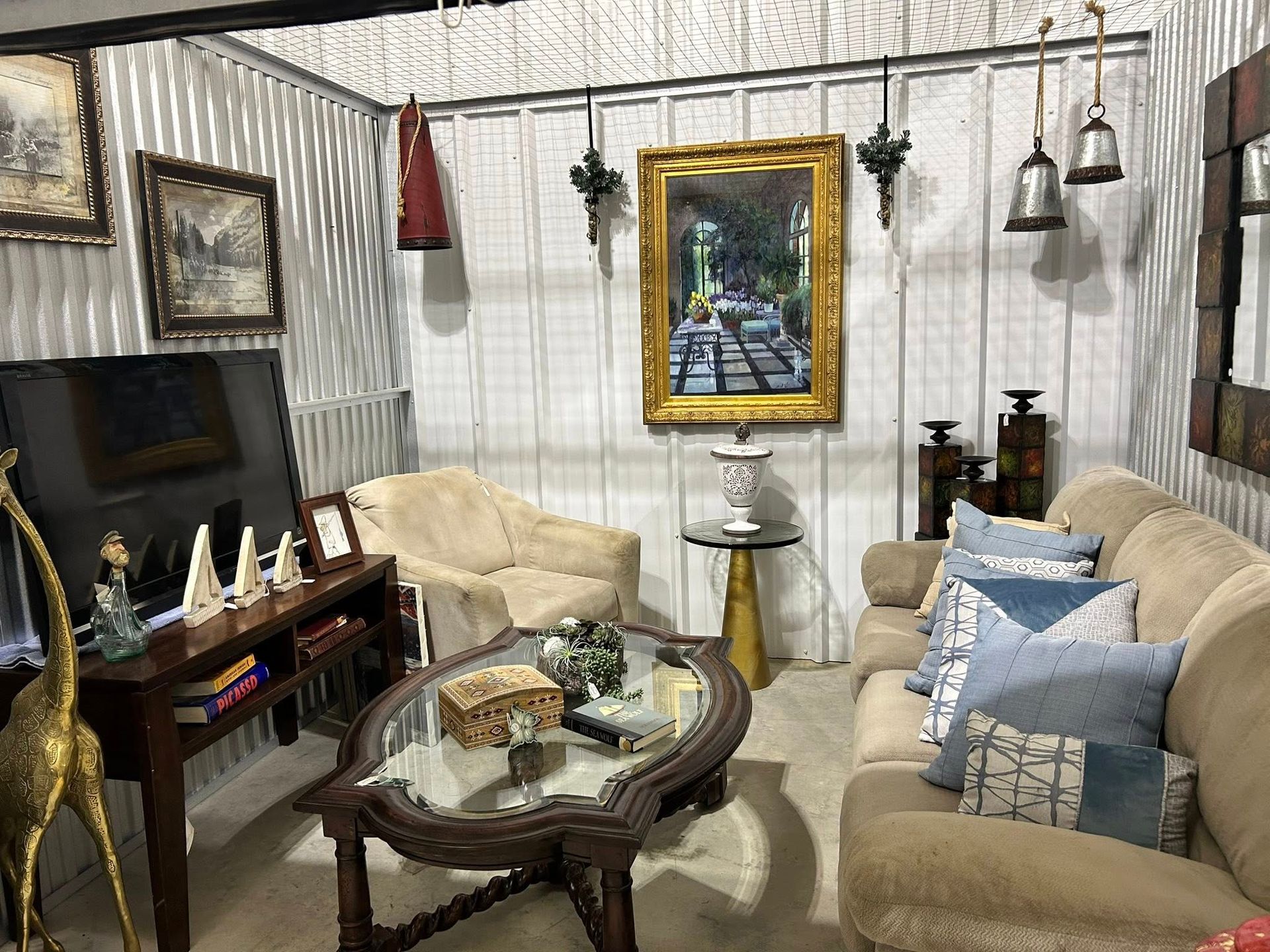 Living room with mismatched furniture, artwork, and decorative objects against corrugated metal walls.