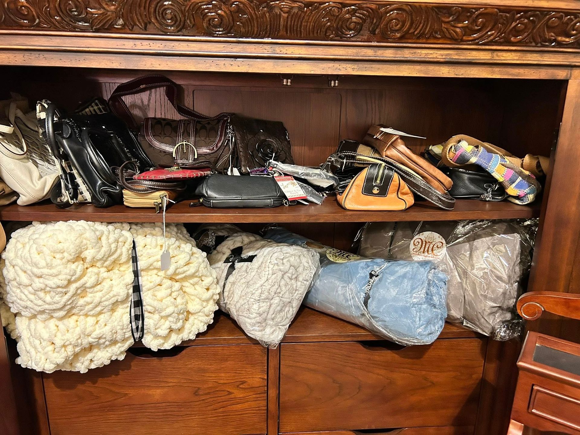 Wooden cabinet filled with purses on top shelf and rolled fabric items on the lower shelf.