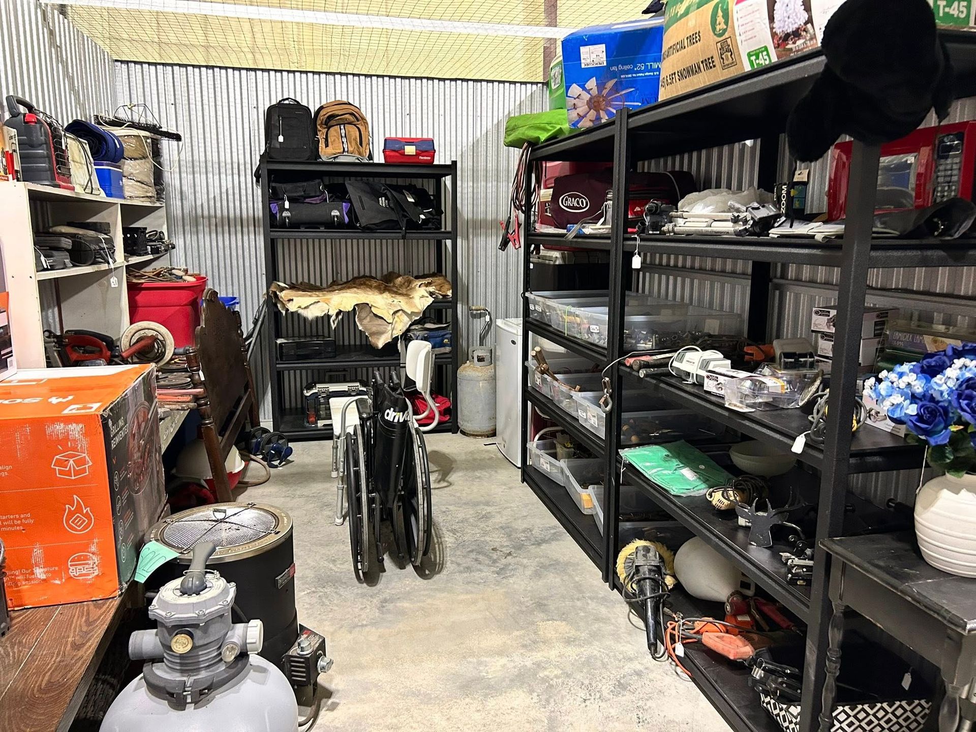 Cluttered storage room with metal shelving holding various items; a folded bike stands in the middle.