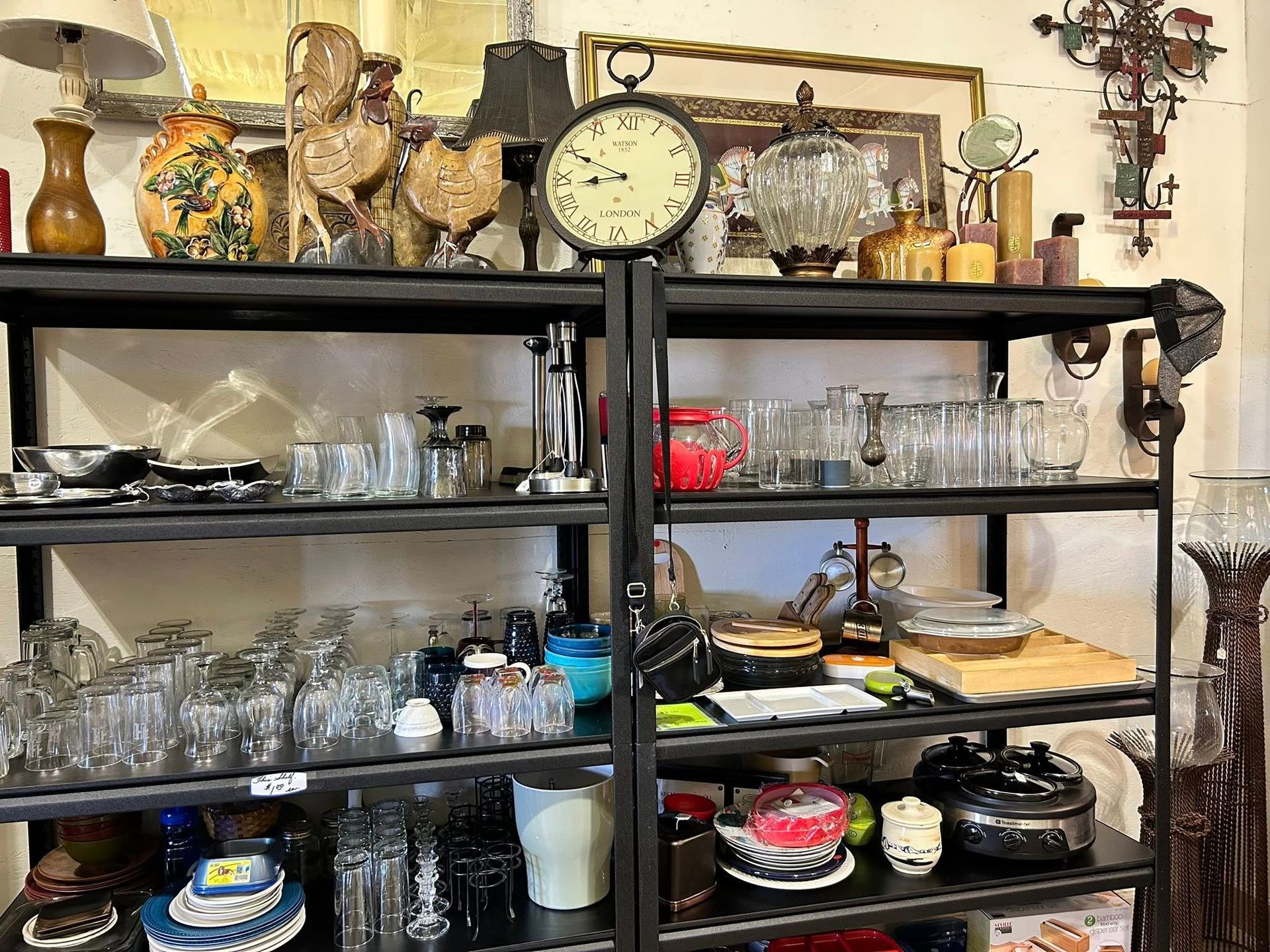 Shelves filled with vintage items: glassware, clocks, lamps, decorative objects in a store setting.