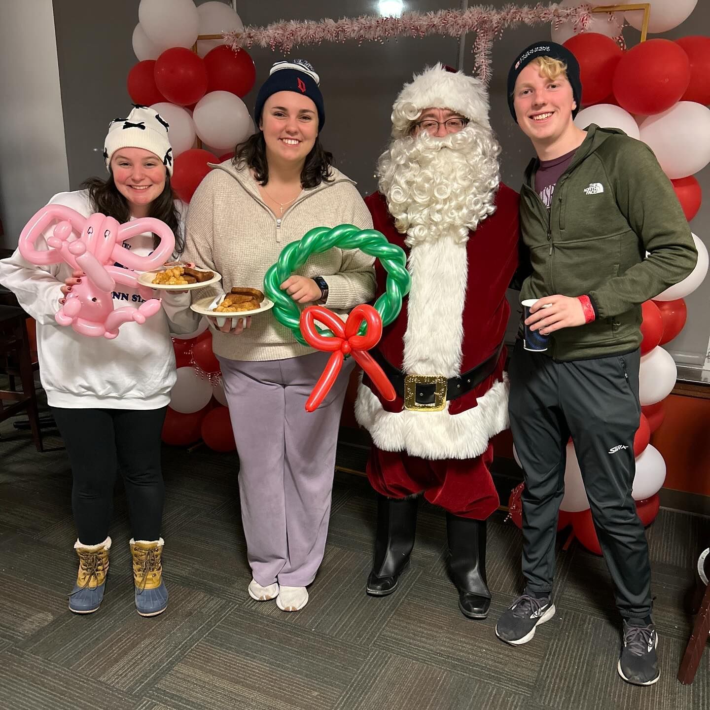 Three people with balloon art, smiling for a photo with Santa
