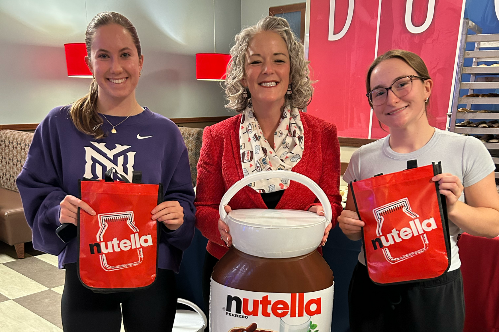 Three women holding Nutella bags and an inflatable Nutella container are smiling for a photo.