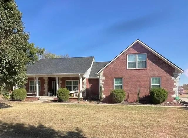Brick house with black roof, white trim, and a porch, set on a brown grassy lawn under a blue sky.