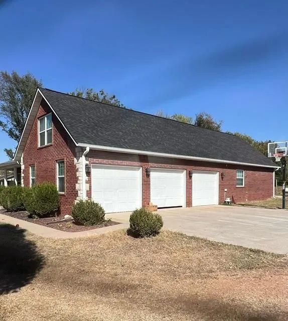 Three-car brick garage with a black roof and white garage doors under a clear blue sky.