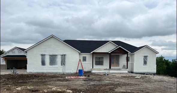 White house under construction, dark roof, cloudy sky, construction materials visible.