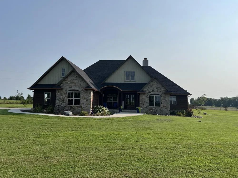 Stone-faced ranch home with dark roof on a grassy plain under a clear sky.