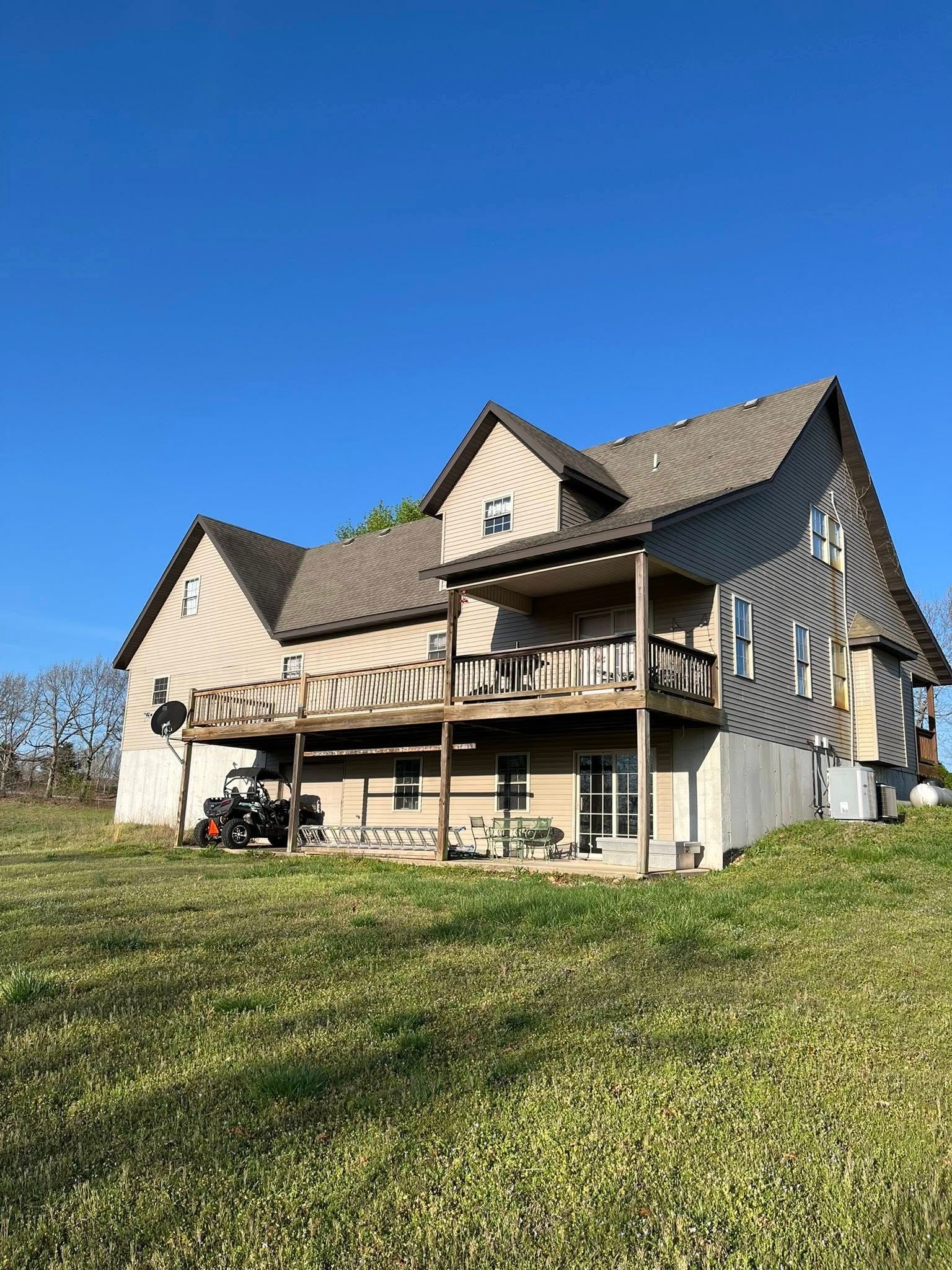 Two-story house with a wooden deck and tan siding under a clear blue sky.