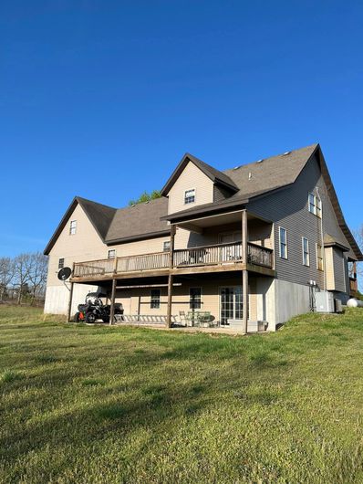 Two-story house with a wooden deck and tan siding under a clear blue sky.