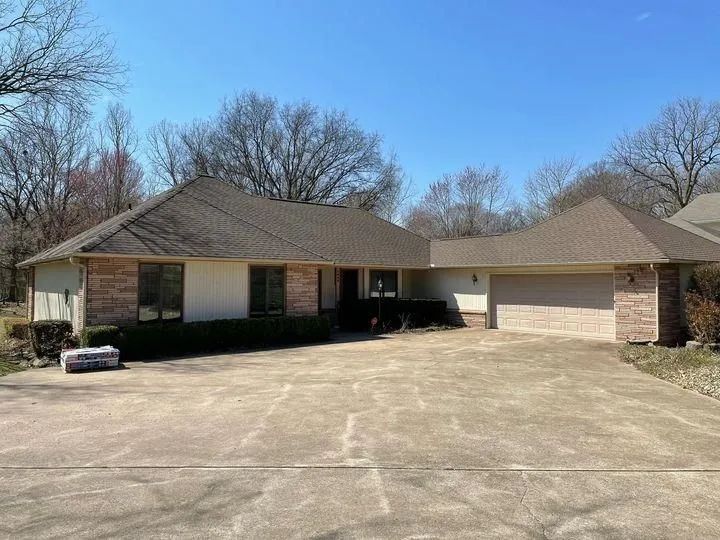 Ranch-style house with brick accents, tan siding, and a concrete driveway on a sunny day.