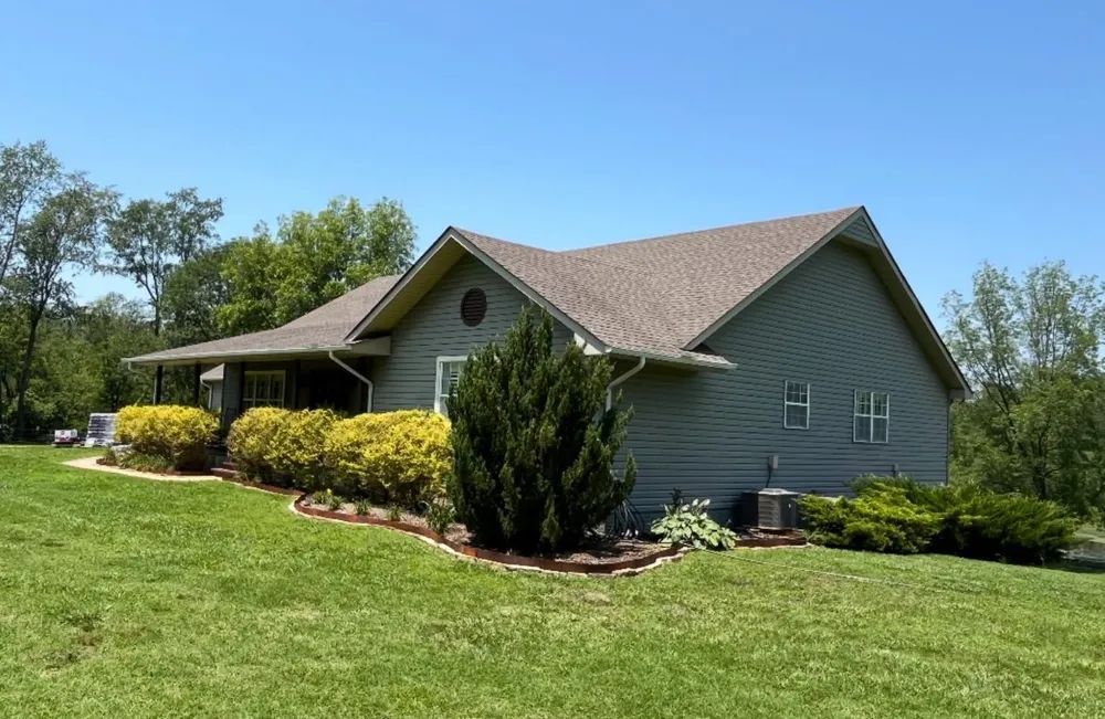 Blue-green house with brown roof and landscaping under a clear, blue sky.
