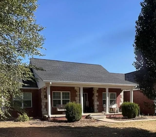 Red brick house with a porch, white columns, and a dark gray roof under a blue sky.