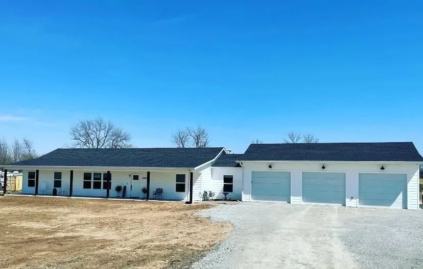 White house with black roof and three-car garage with light blue doors under a clear blue sky.