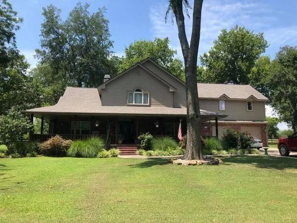 A two-story brown house with a large front porch and green yard under a blue sky.