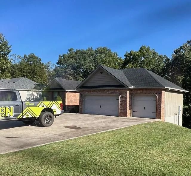 A truck with a trailer parked in a driveway in front of a house with a two-car garage.