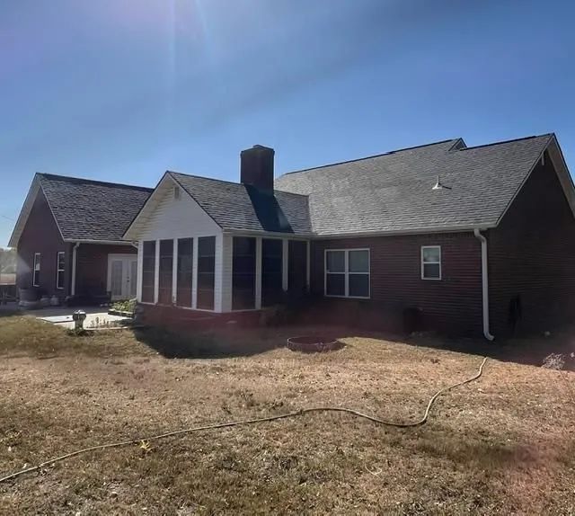 A brick house with a dark roof and a screened-in porch, on a sunny day.
