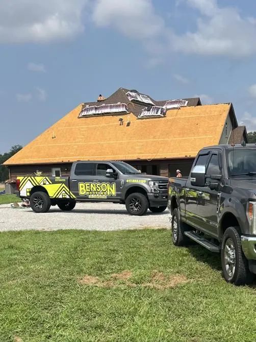Two work trucks parked in front of a house under construction; roof partially complete.