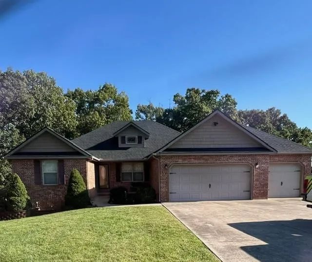 Brick house with a three-car garage, green lawn, and blue sky.