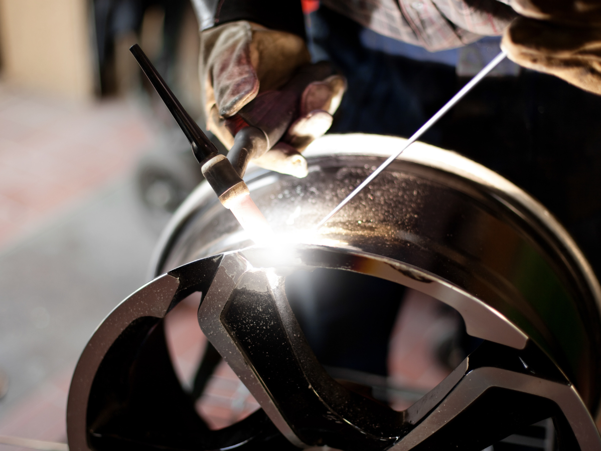 Welder using a torch to repair a black and silver car wheel. Sparks fly as he works.
