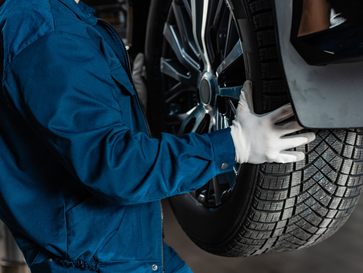 Mechanic in blue coveralls and white gloves checks a car tire.