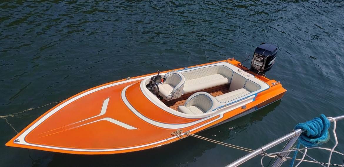 A small orange and white boat is floating on top of a body of water.