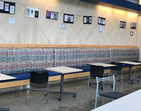 A row of tables and chairs in a room with pictures on the wall