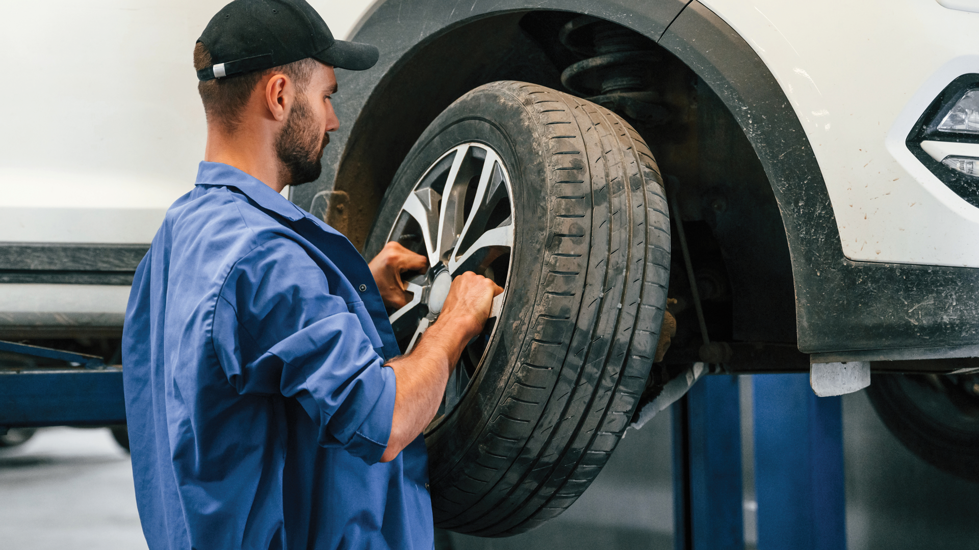 A man is changing a tire on a car on a lift.