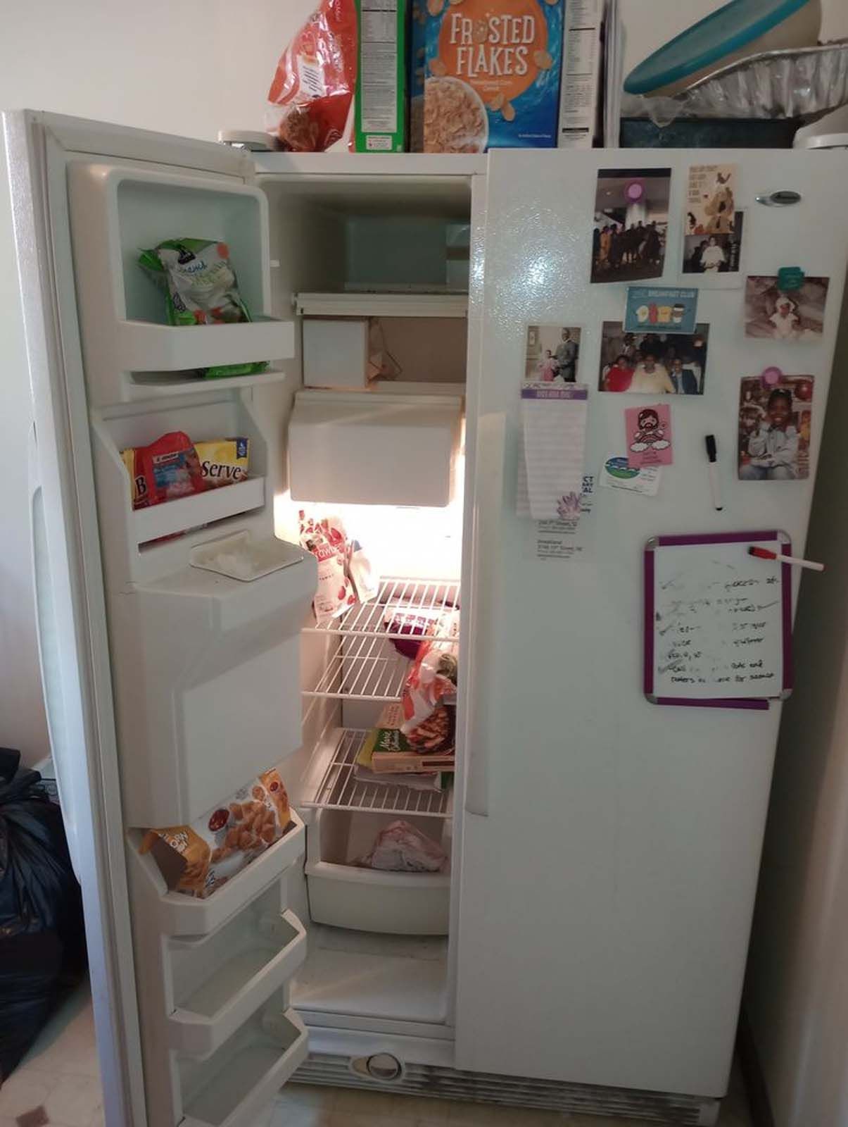 A refrigerator with the door open and a box of frosted flakes on top of it.