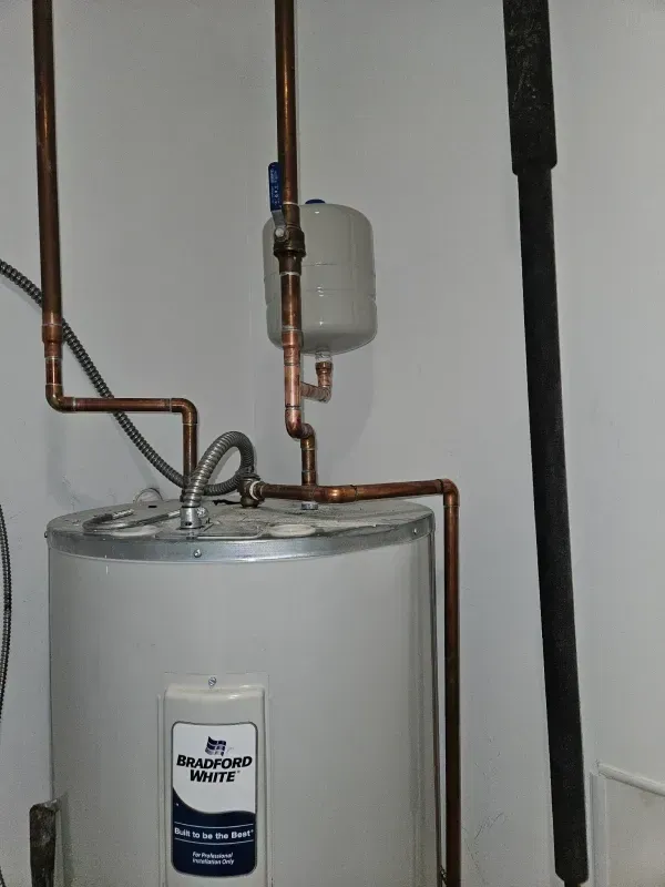 A Bradford White water heater with copper pipes in a white-walled room.