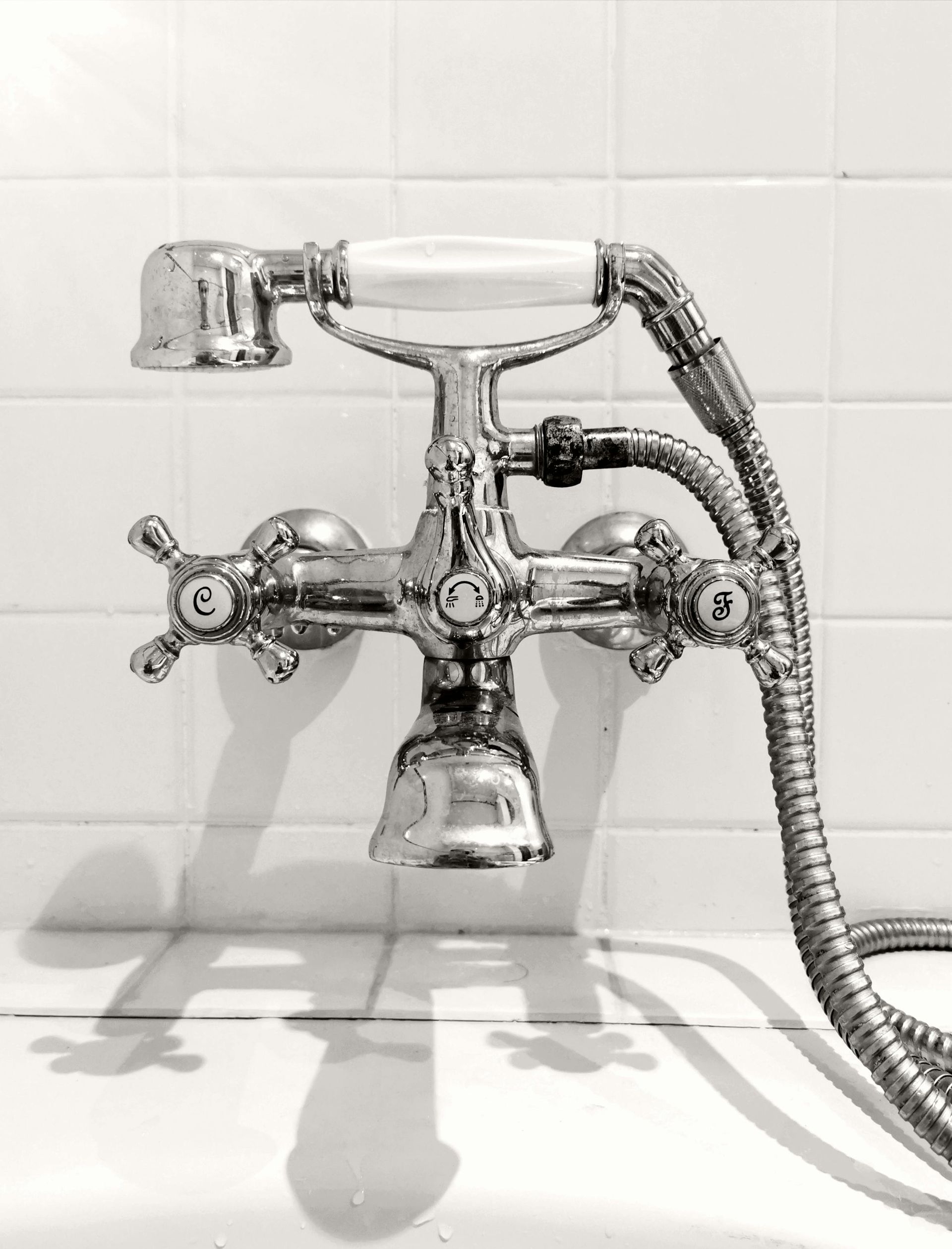 Chrome shower faucet with hand-held sprayer, set against white tiled wall.