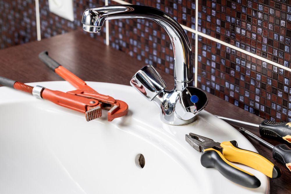 Bathroom sink with tools, faucet, and brown and blue tile backsplash.