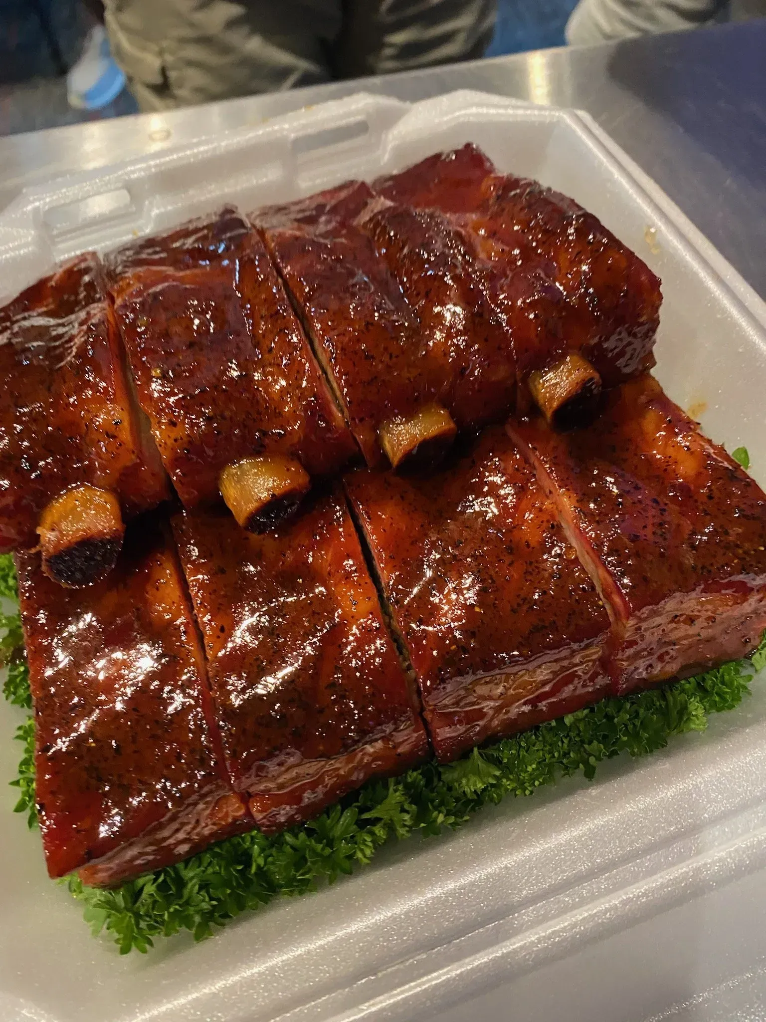 A styrofoam container filled with ribs and lettuce on a table.