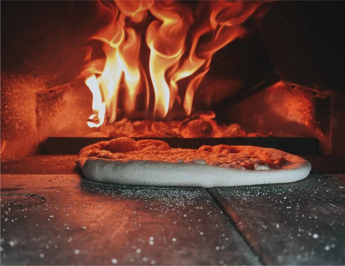 A pizza is being cooked in an oven with flames coming out of it.